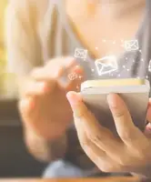 Personne utilisant un smartphone, avec des icônes d’e-mails flottant au-dessus de l’écran. Credits-Monster-Ztudio